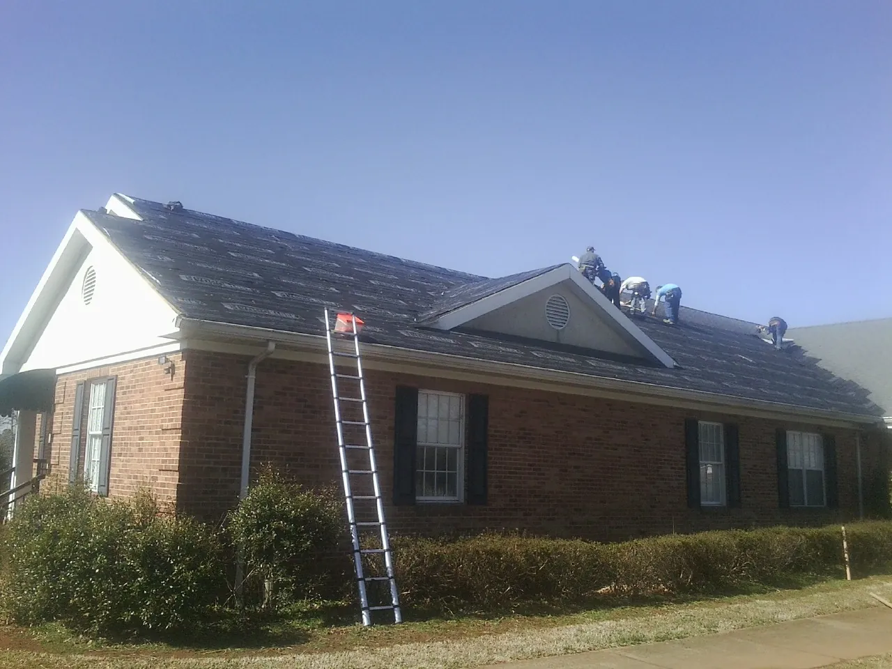 Crew tearing shingles off a brick ranch roof with a ladder set — Metal Roof Repair work by our crew in Tremont