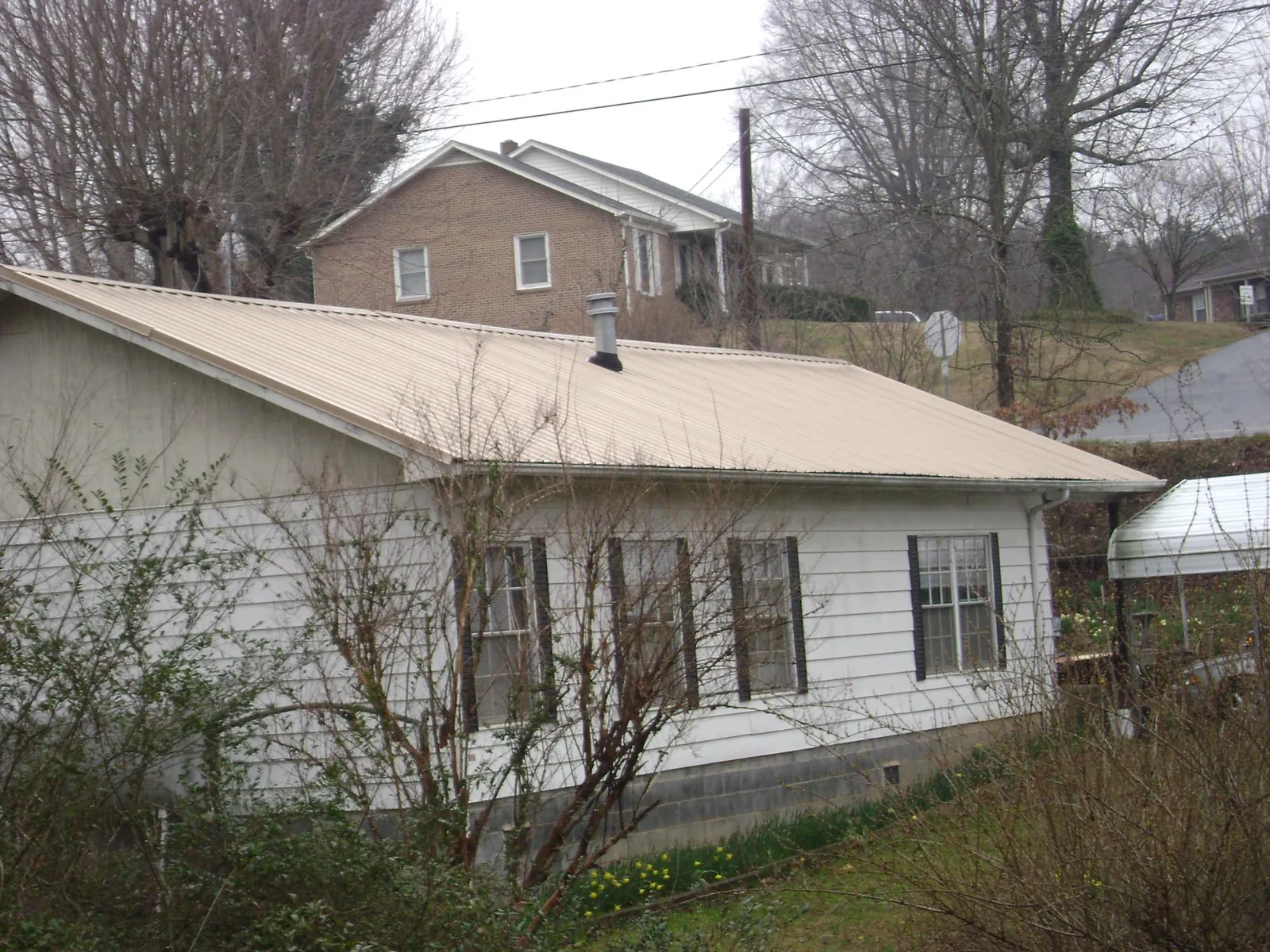 Tan metal roof on a white sided house set into a hillside — Commercial Roofing by Roofing Brothers in Tremont