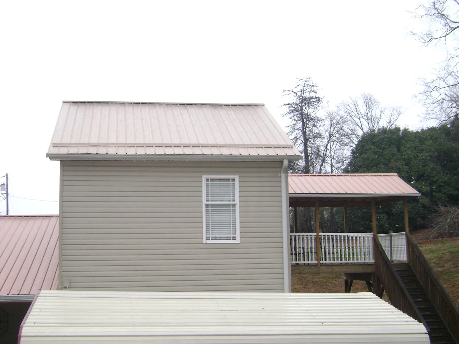 Tan metal roofs on a two story addition and attached porch, from a Roof Replacement job in Tremont